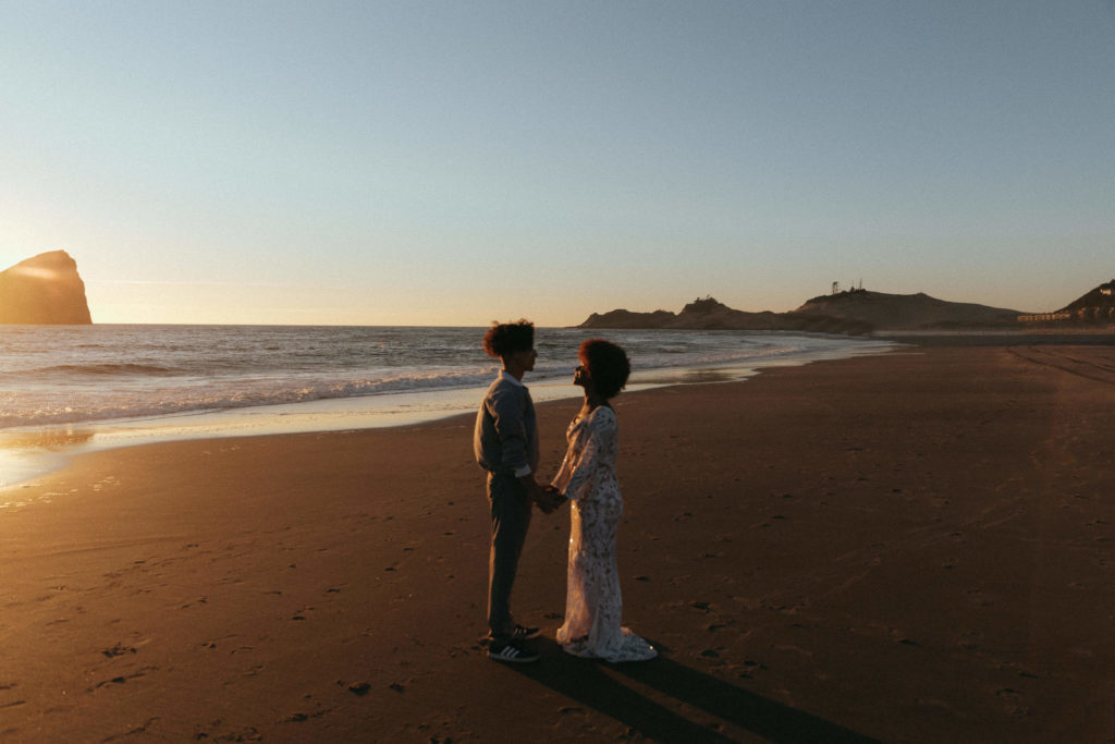 A couple planning to elope on the Oregon Coast enjoying the sunset on the beach together.