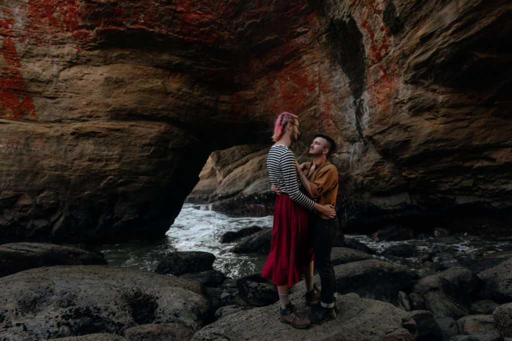 A couple embracing in the middle of the Devil's Punchbowl while standing on rocks with waves crashing around them