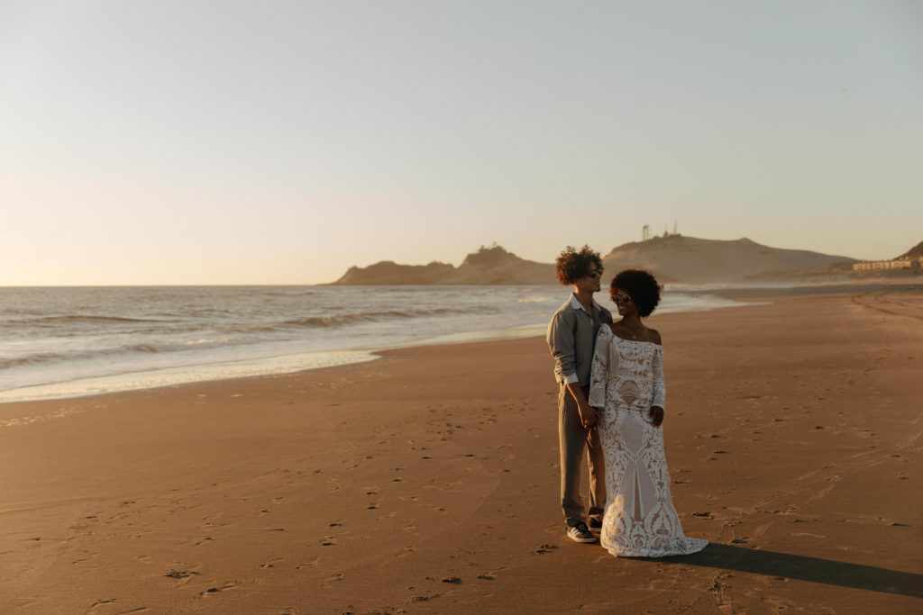 Retro couple standing on the beach at Cape Kiwanda in Oregon after their elopement at sunset 