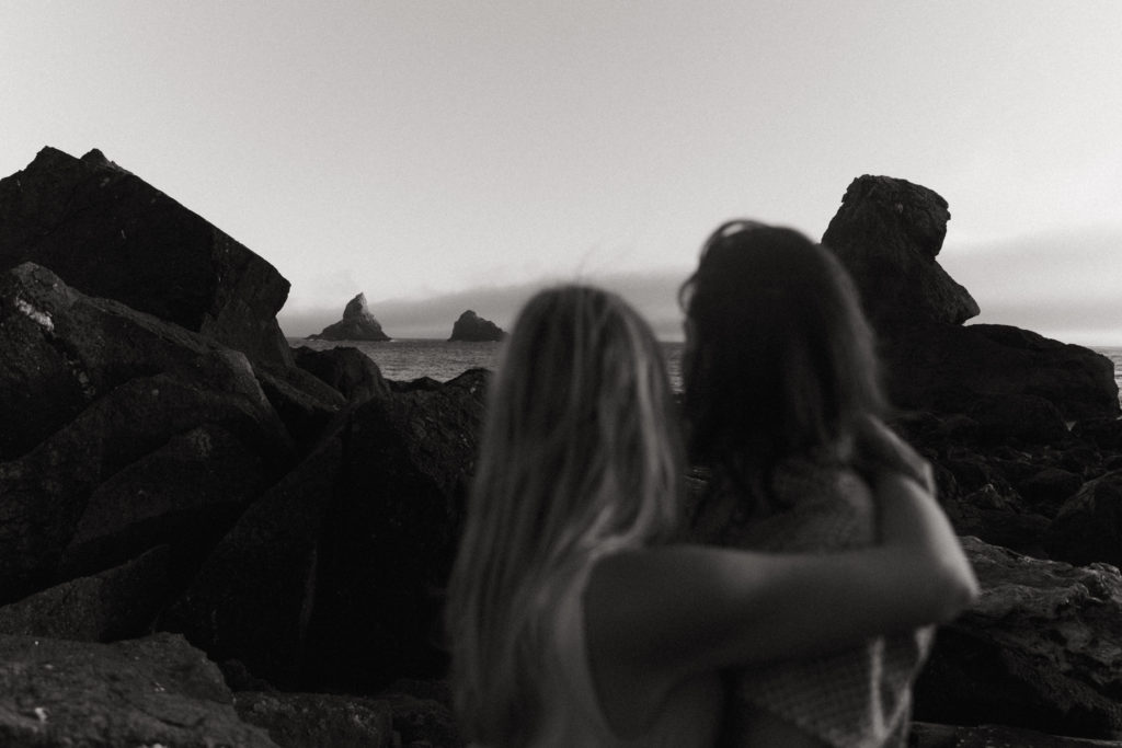 Couple holding eachother and gazing out at rock formations on the Oregon Coast at sunset 