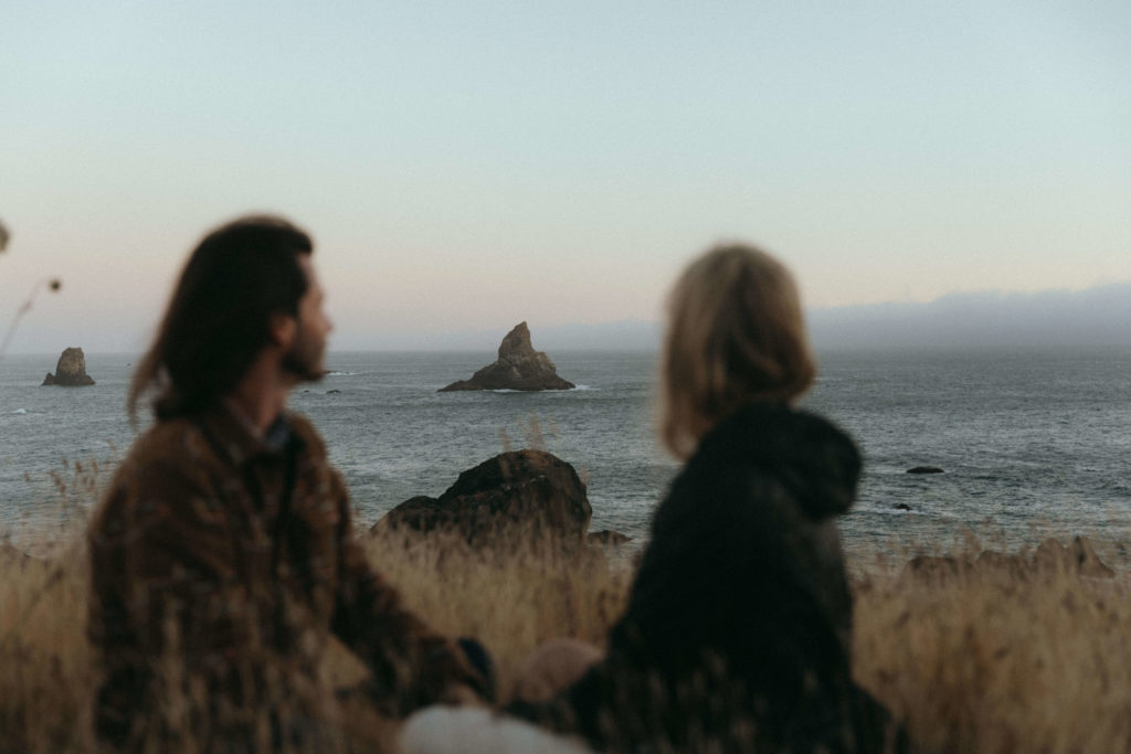 Couple gazing off at rock formations of a cliff on the Oregon Coast at sunset 