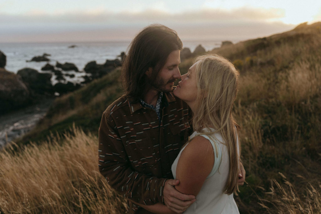 Couple kissing at sunset while standing on a cliff on the Oregon Coast after their engagement photos 