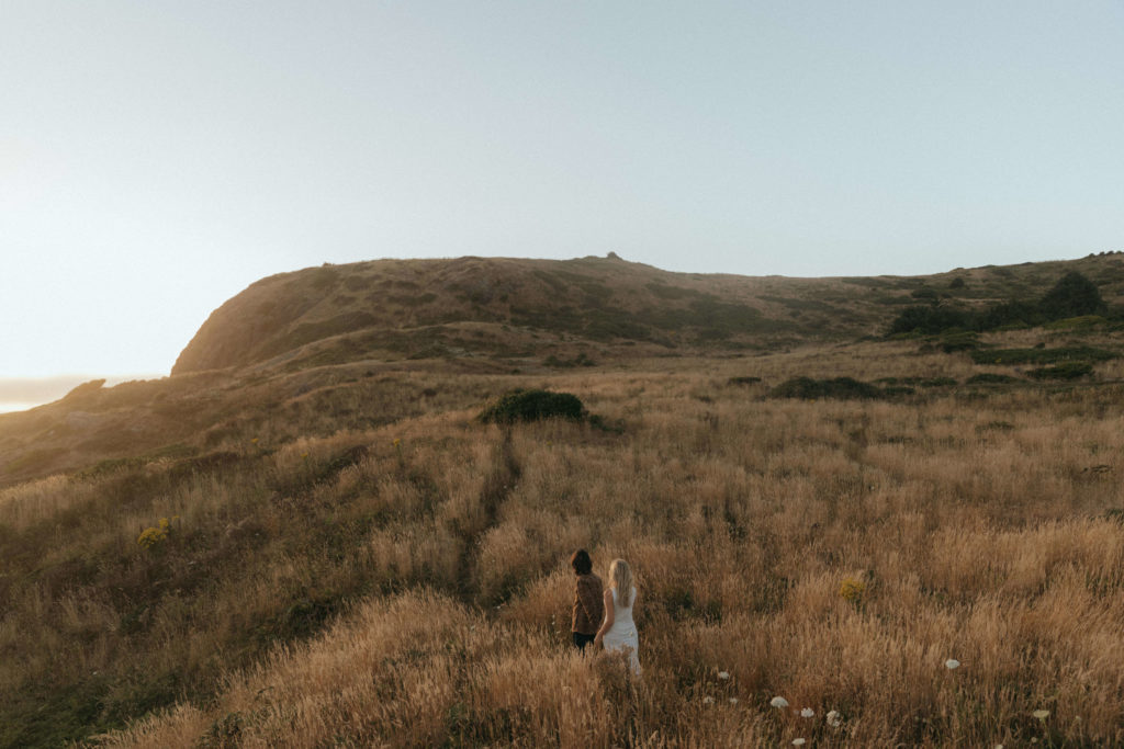 Couple walking through a field of tall grass along the Oregon Coast at sunset 