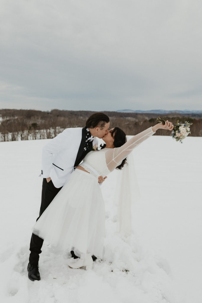 Couple kissing in the snow holding hands together after their winter elopement in the mountains 