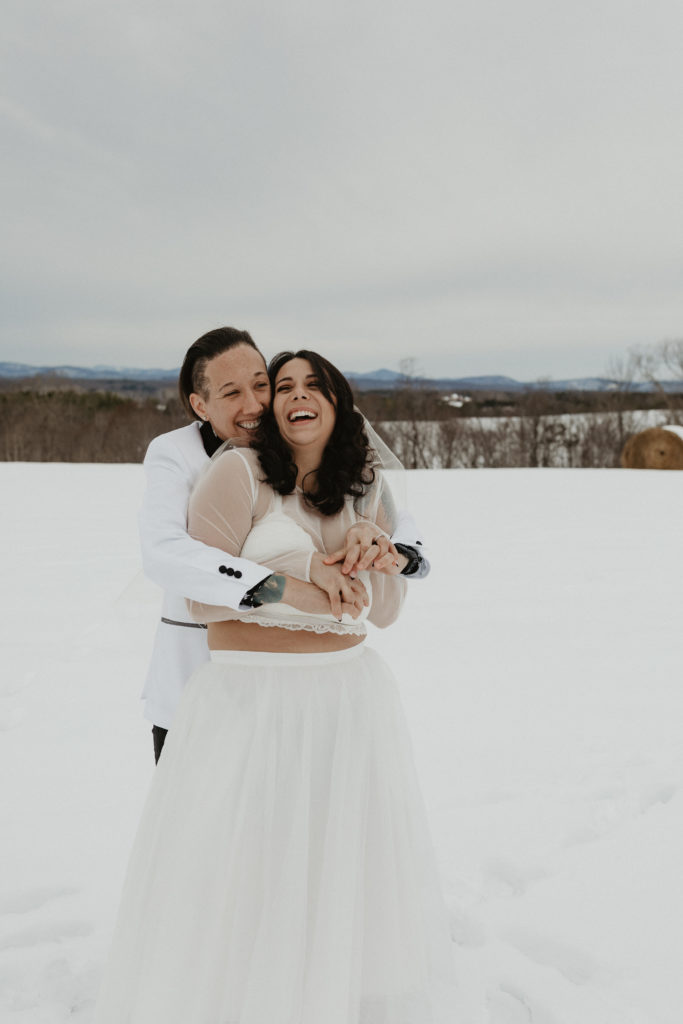 Couple standing in the snow laughing together after their winter elopement in the mountains 