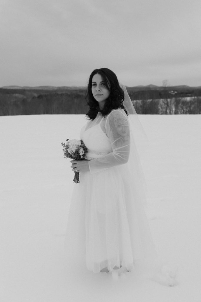Bride standing in the snow holding smiling after a winter elopement in the mountains 