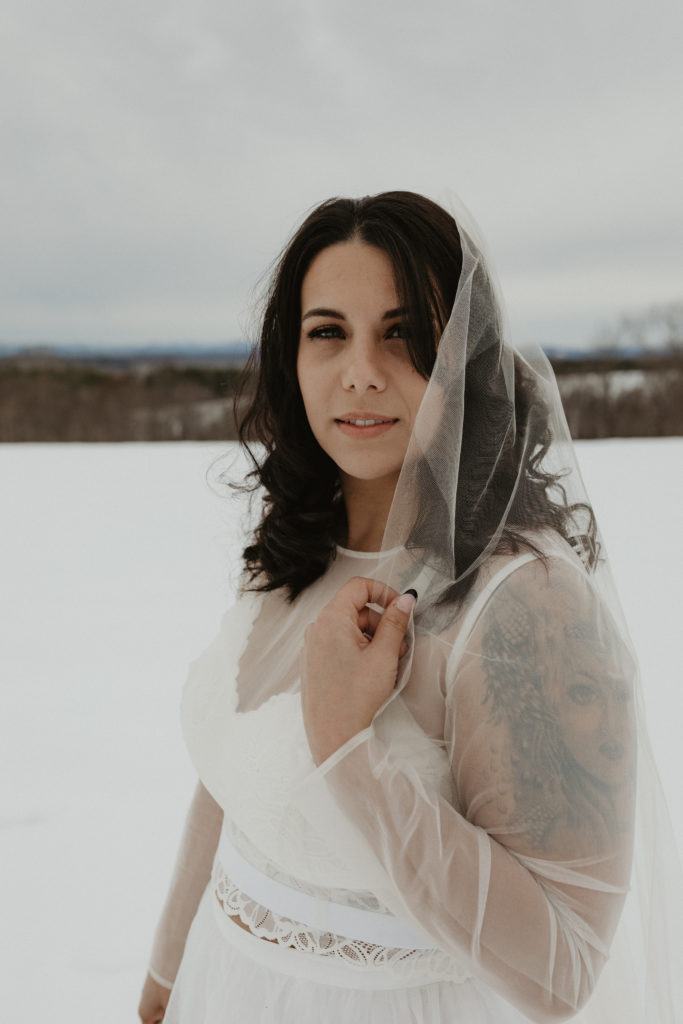 Bride standing in the snow holding smiling after a winter elopement in the mountains 